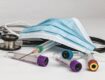 A stethoscope, medical mask, and various laboratory test tubes scattered on a white surface