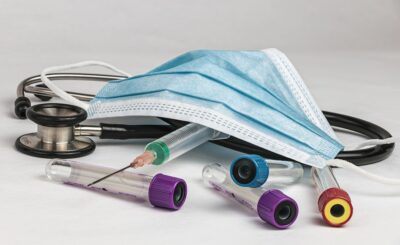 A stethoscope, medical mask, and various laboratory test tubes scattered on a white surface