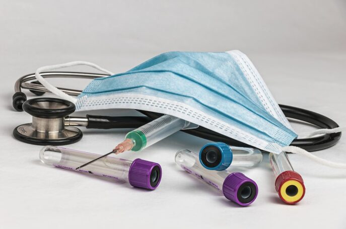 A stethoscope, medical mask, and various laboratory test tubes scattered on a white surface