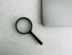 A magnifying glass placed on a marble surface next to a laptop