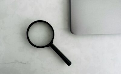 A magnifying glass placed on a marble surface next to a laptop
