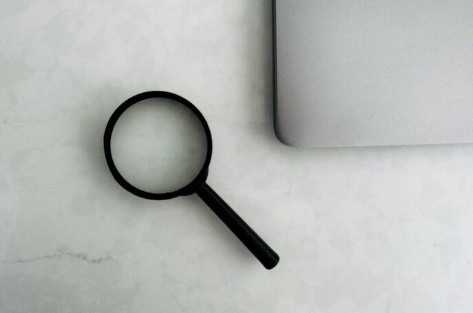 A magnifying glass placed on a marble surface next to a laptop