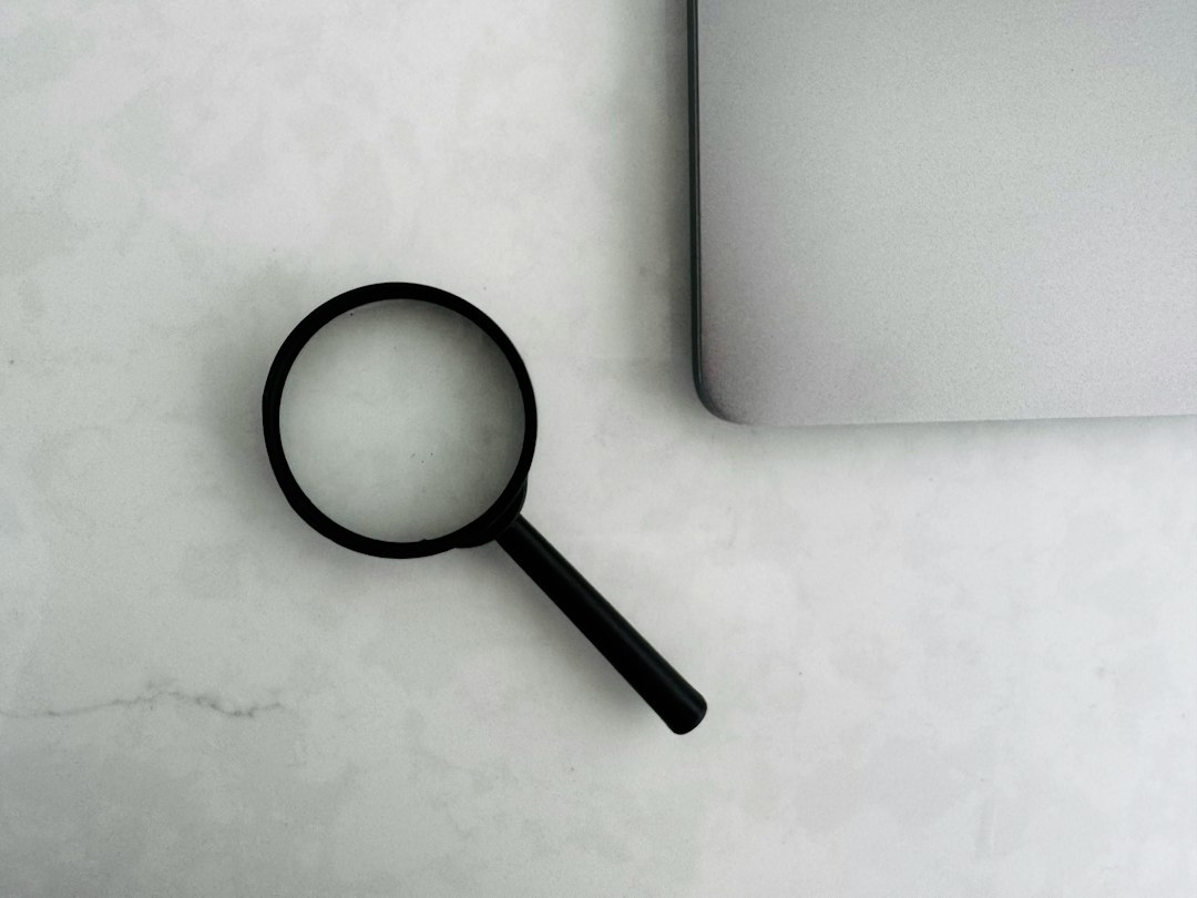 A magnifying glass placed on a marble surface next to a laptop